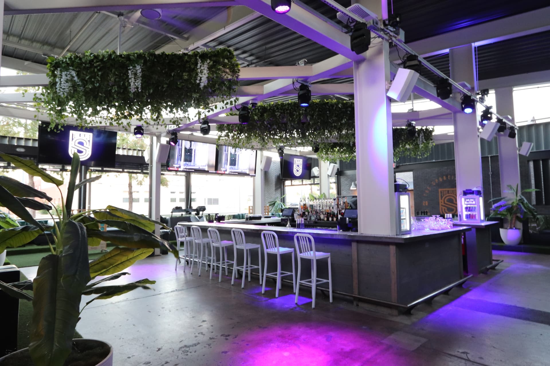 Sporting Club main bar beneath hanging greenery with the club logo on screens.
